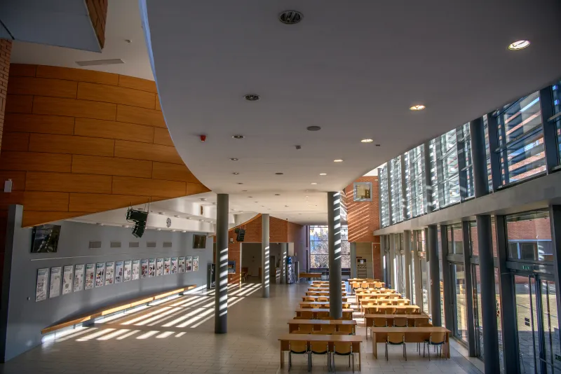 The Aula of Óbuda University: a bright, high-ceilinged hall with glass walls, a curved wooden gallery and rows of tables